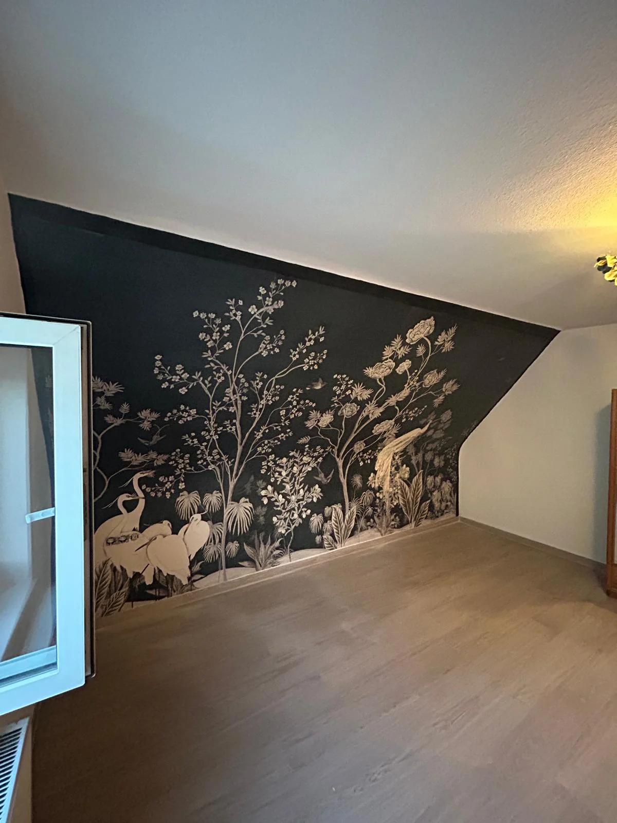 Dunkle Motivtapete mit Pflanzen- und Tiermotiven an einer Wand unter einer Dachschräge.