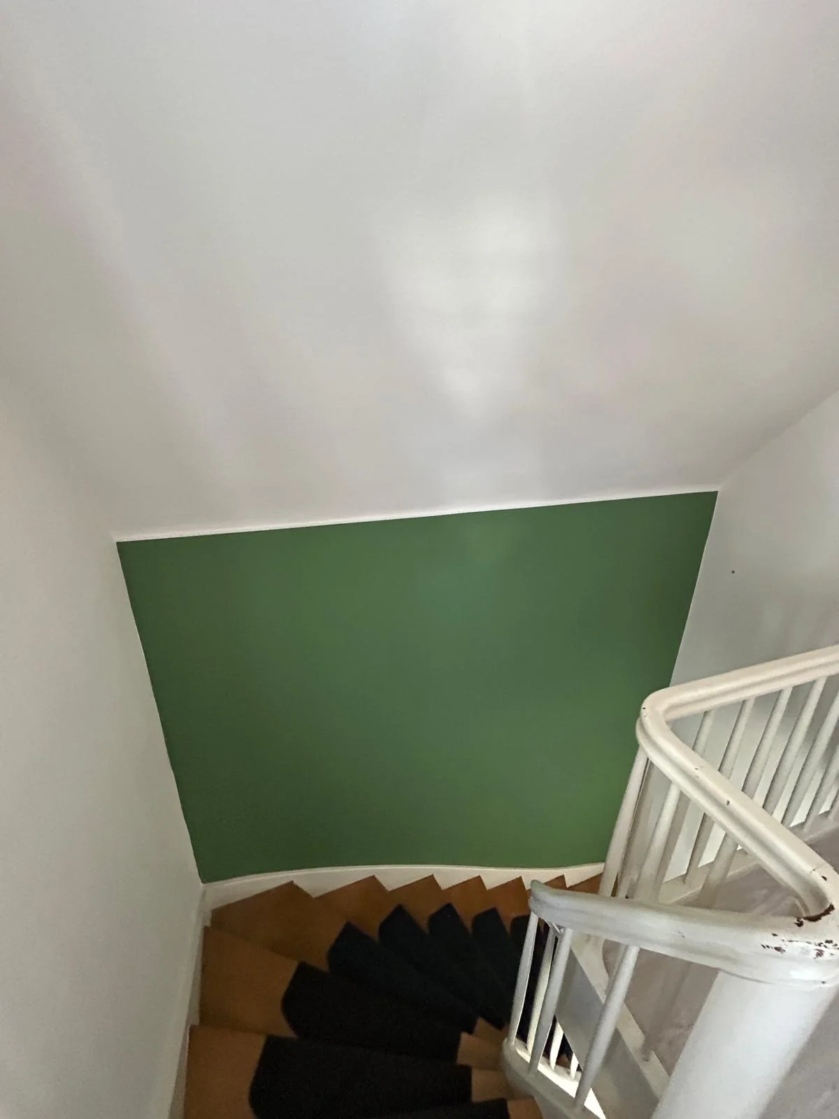 Grüne Akzentwand neben einer weißen Treppe und hellen Wandflächen.