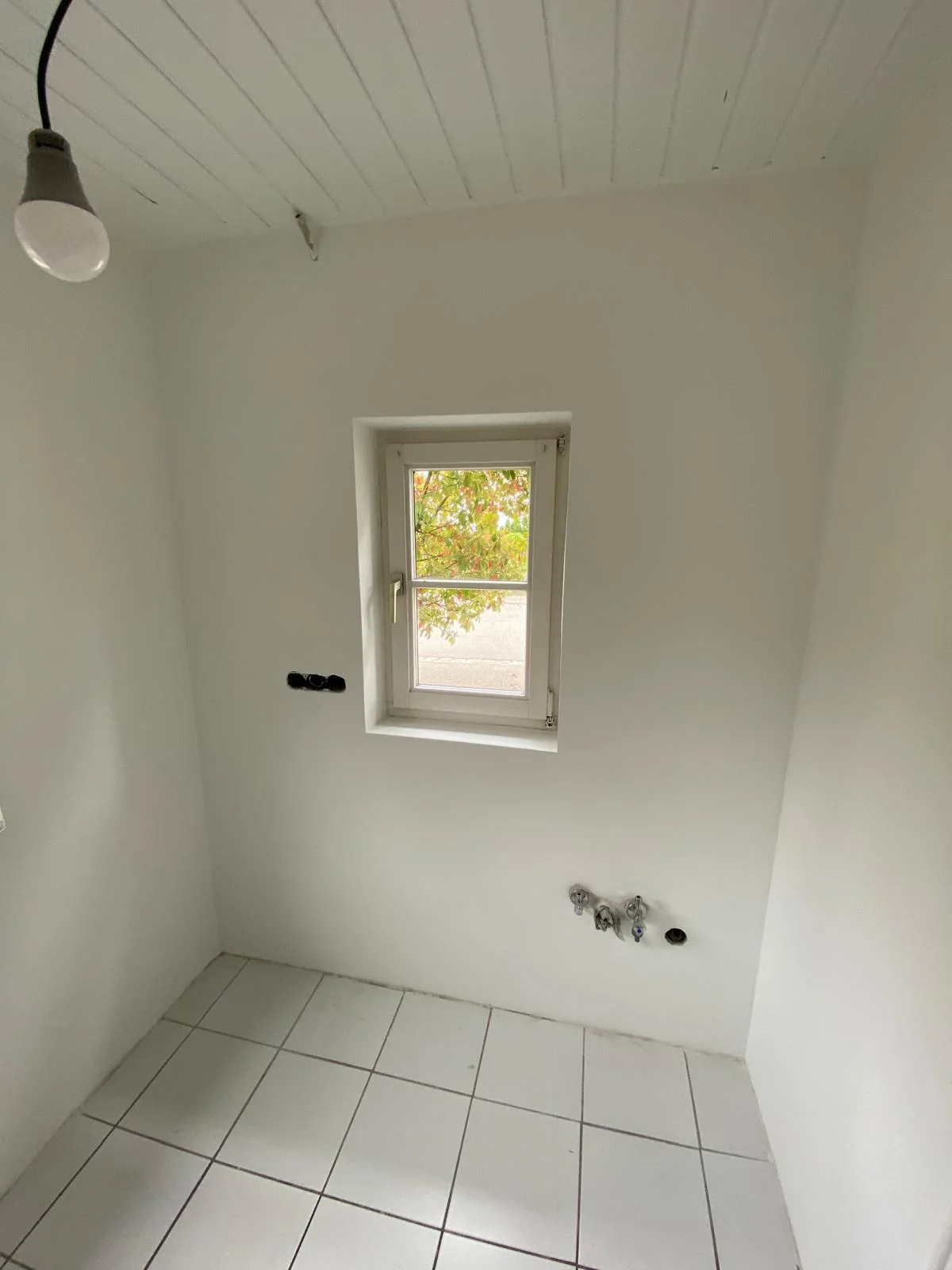 Heller Raum mit weißer Wand, kleinem Fenster und Paneeldecke.